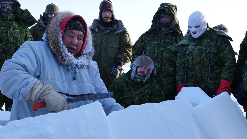 Un homme derrière des blocs de neige entouré par des militaires. 