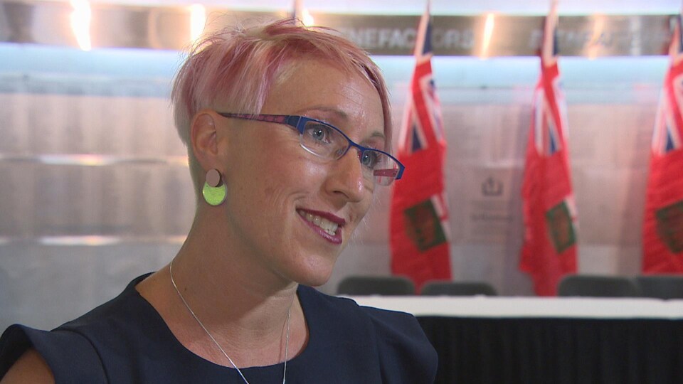 Une femme s'adresse à la caméra alors qu'en arrière-plan on distingue des drapeaux.