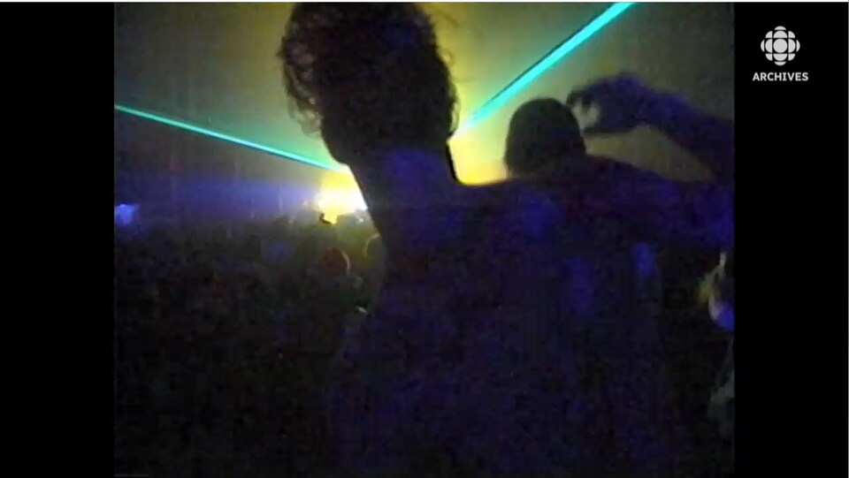 Homme de dos devant un faisceau de lumière qui danse parmi un large groupe dans un rave.