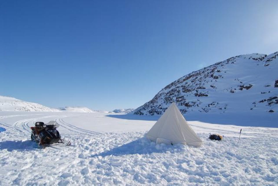 Une tente et une motoneige dans un paysage hivernal désolé.