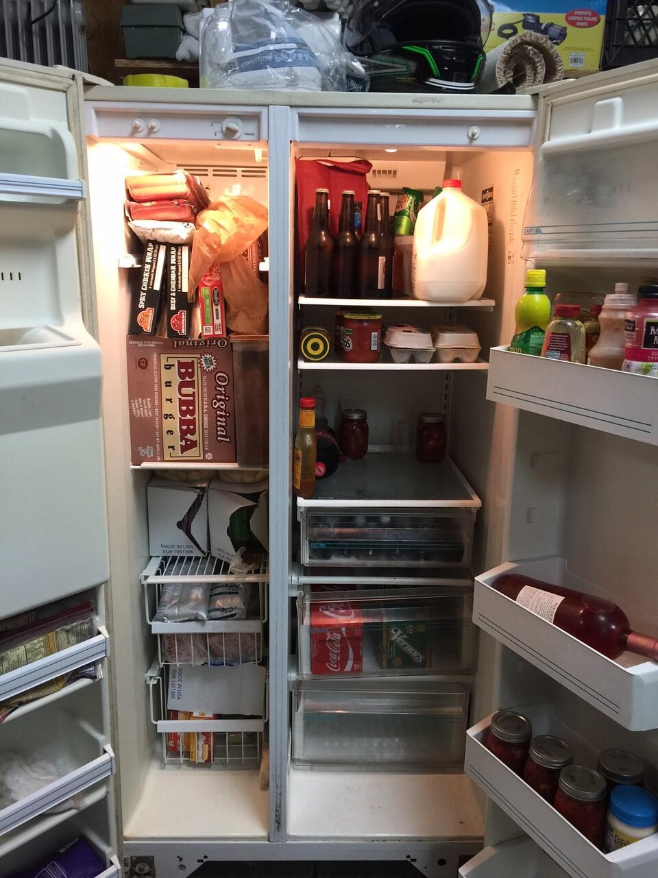 Un réfrigérateur qui semble plein et qui est notamment rempli de condiments, de bouteilles de bière et de vin, d'oeufs et de lait.