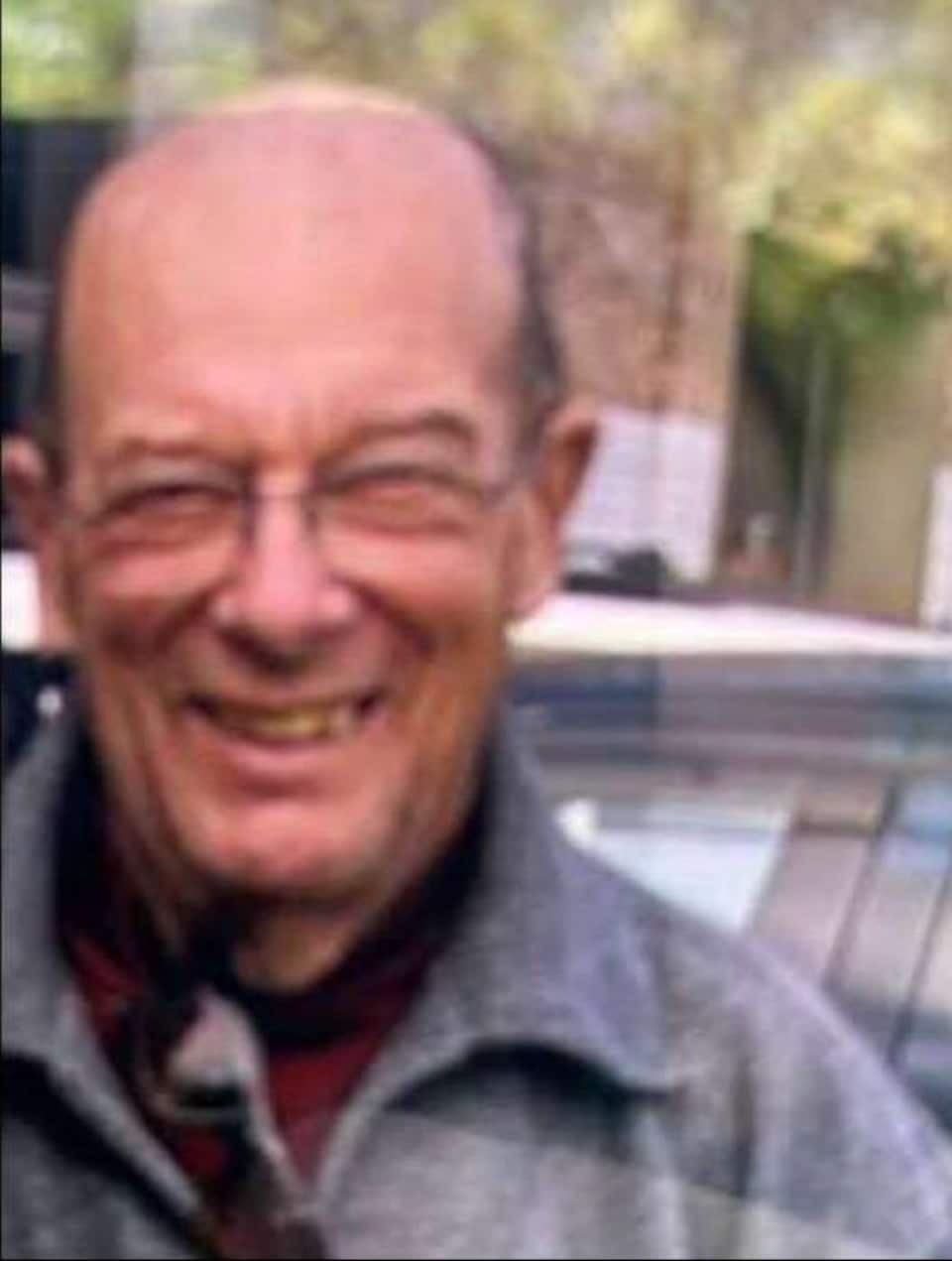 A fairly blurry photo of a smiling septuagenarian for an outdoor photo.