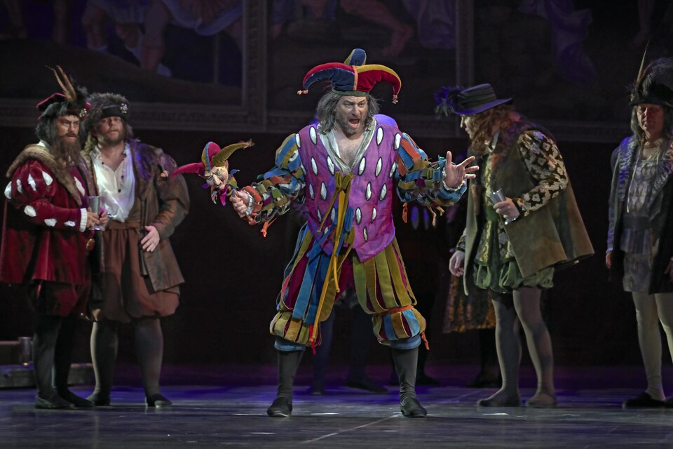 Des hommes costumés en un fou du roi et des sujets de la cours sont sur une scène.