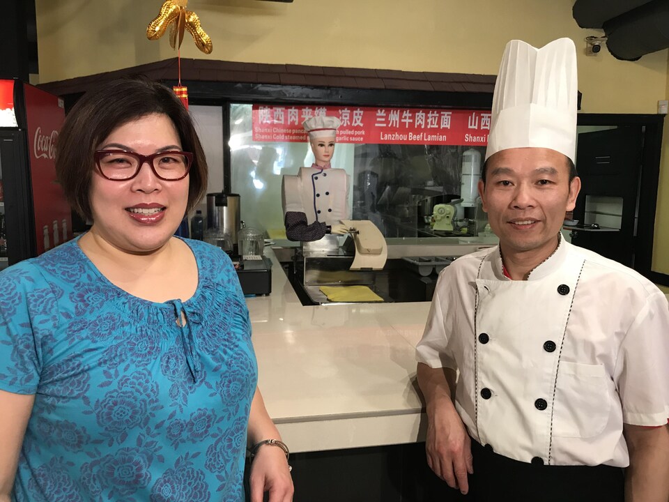 Le propriétaire et chef cuisinier, Hank Ren, et la gérante Cindy Tsang posent devant le robot qui se trouve derrière un comptoir. 