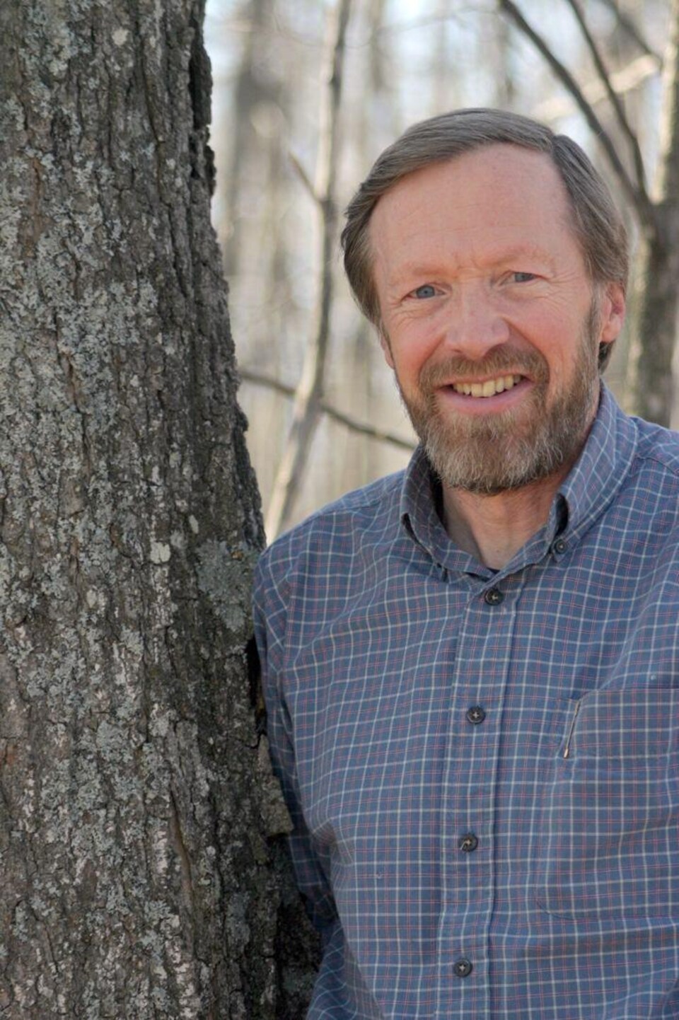 Un homme en chemise carrelée debout contre un arbre