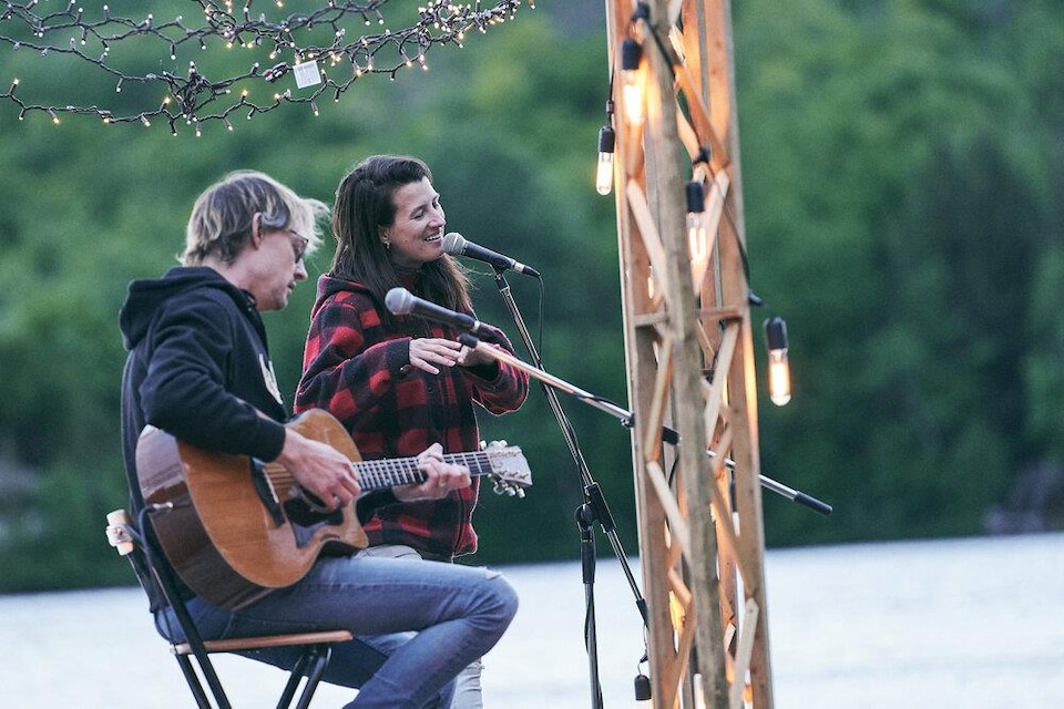 Un chanteuse et un homme avec une guitare font une prestation sur un quai flottant au milieu d'un lac. 