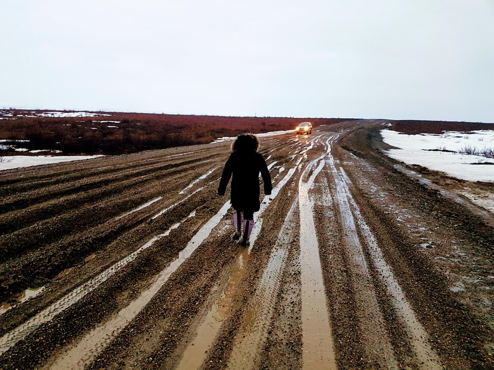 Une femme marche sur la route boueuse. 