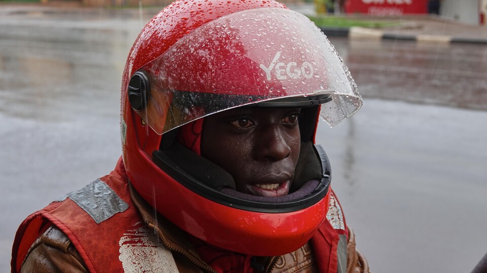 Un homme vêtu d'un habit de cuir et d'un casque de moto attend sous la pluie.                               