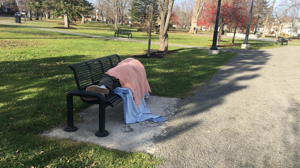 Un homme étendu sur un banc avec des couvertures. 