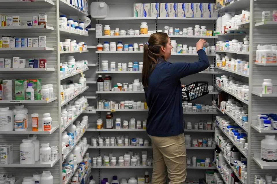 Une employée d'une pharmacie dépose des médicaments sur des tablettes.