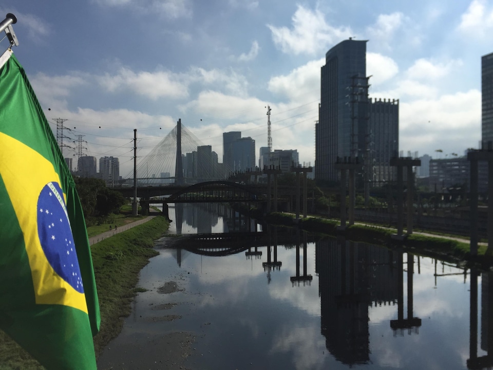Le fleuve Rio Tietê passant sous deux ponts dans la ville de Sao Paulo avec un drapeau brésilien sur la gauche de la photo.