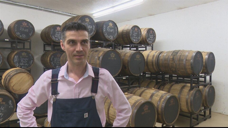 Photo du propriétaire de la distillerie Fils du Roy, Sébastien Roy, devant des barils de rhum et de whisky.