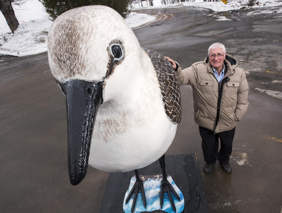 Un homme debout à côté d'une statue d'oiseau plus haute que lui.