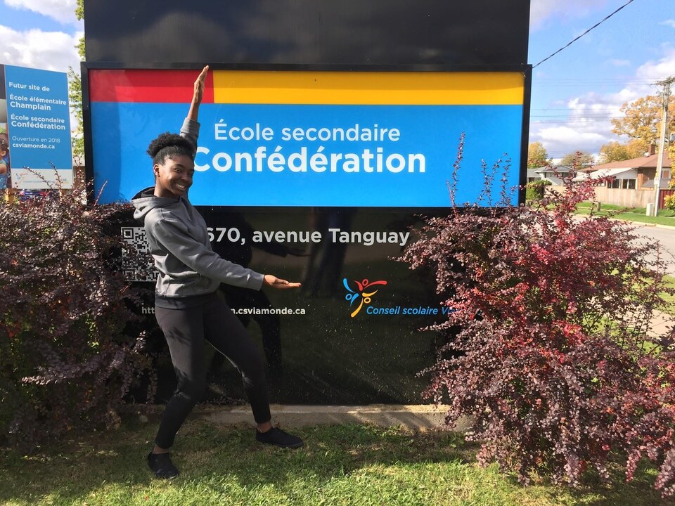Photo de Sherna devant le panneau de l'école