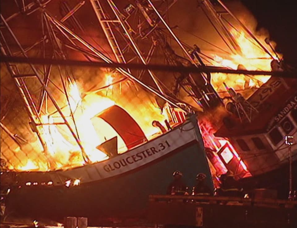 Deux bateaux hauturiers brûlent durant la nuit devant des pompiers.