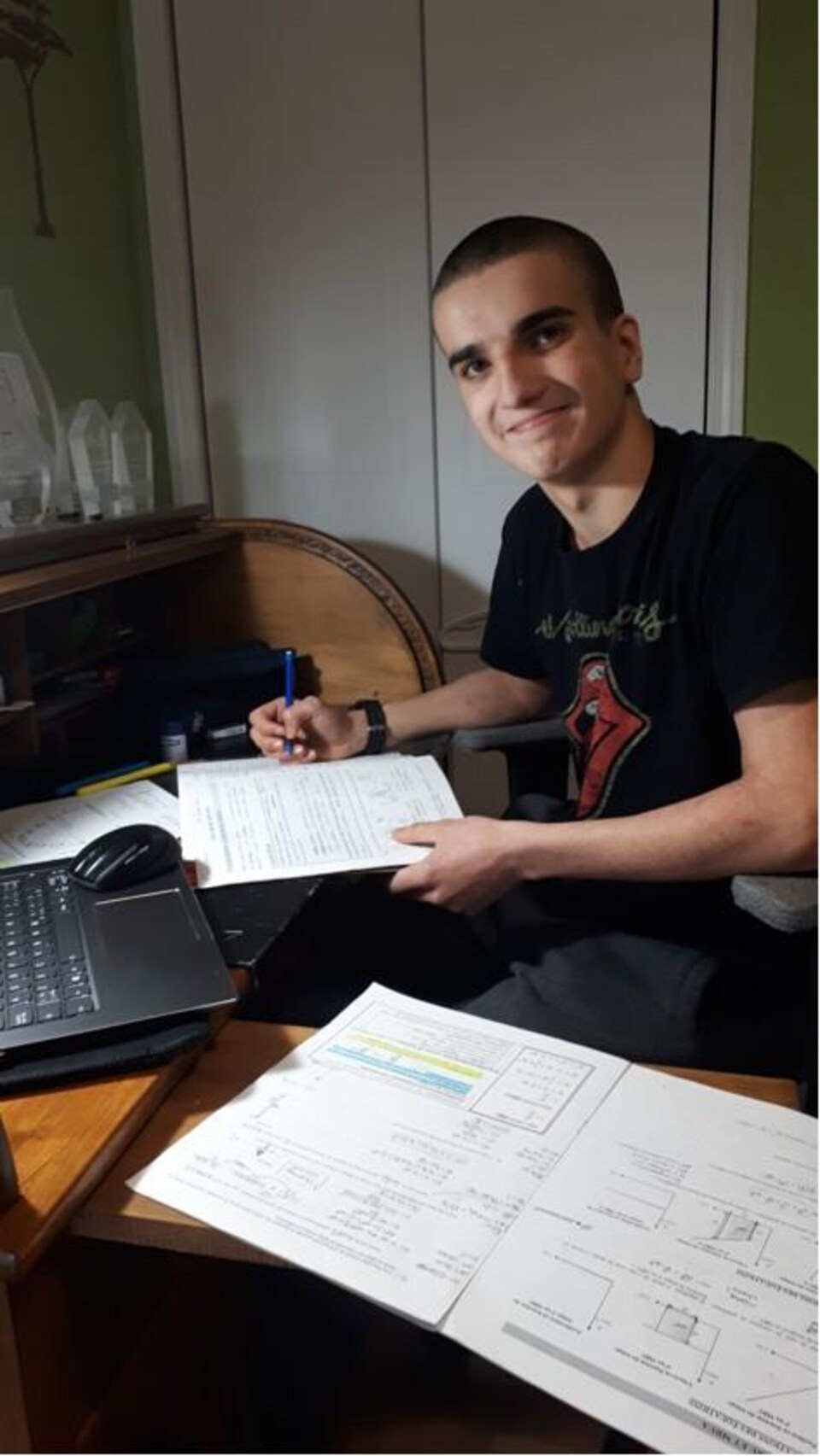 Le jeune homme est devant l'ordi avec ses devoirs.