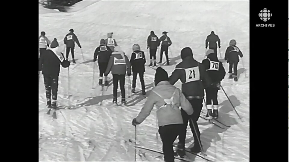 Jeunes avec des dossards qui se déplacent en ski en groupe serré.