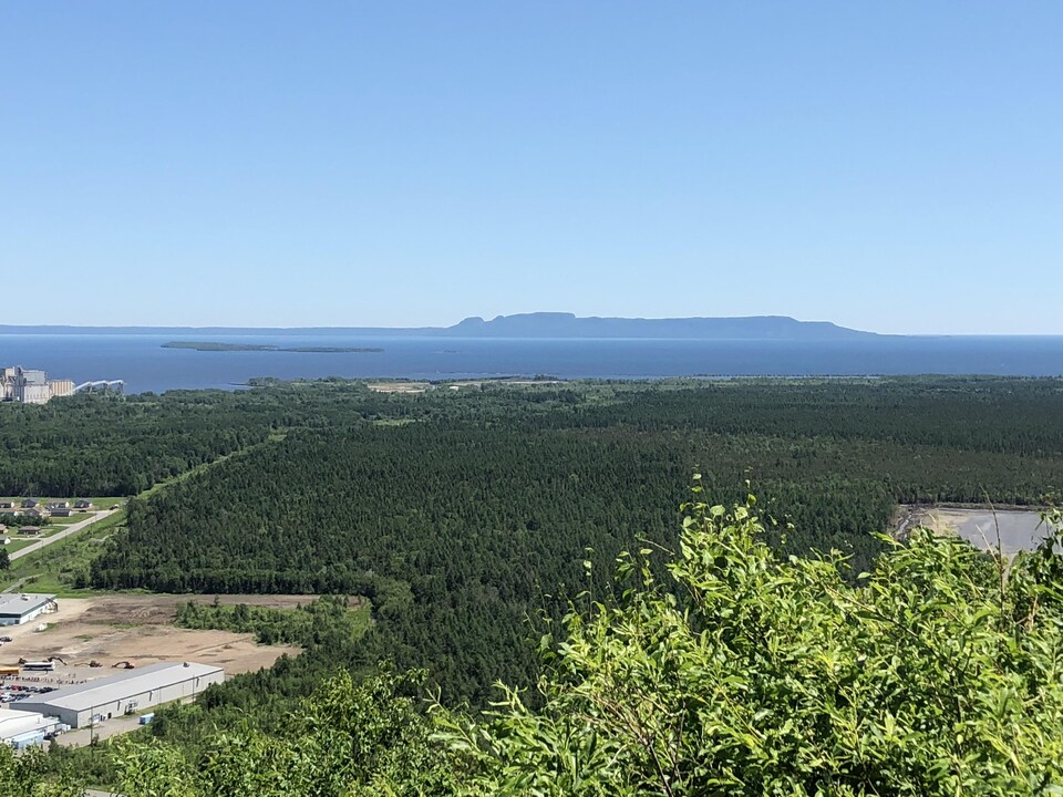 Un paysage de forêt et d'eau avec en arrière plan une péninsule ressemblant à un homme couché sur le dos.