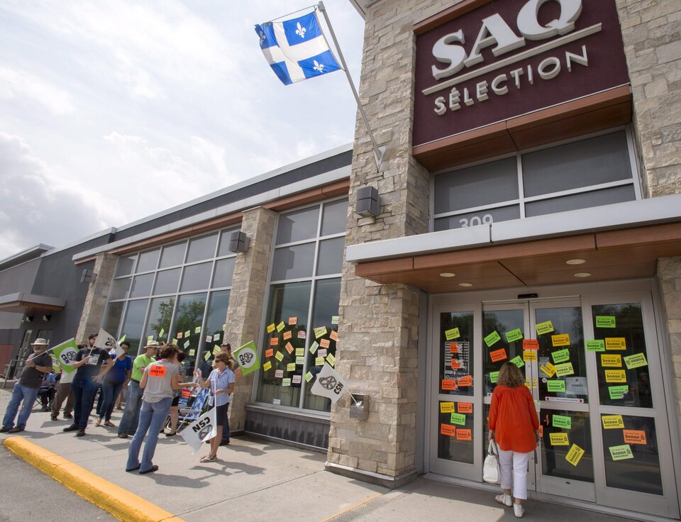 Une cliente se bute à des portes fermées devant un magasin de la SAQ pendant que des syndiqués en grève arborent des pancartes à Rosemère, en banlieue de Montréal 