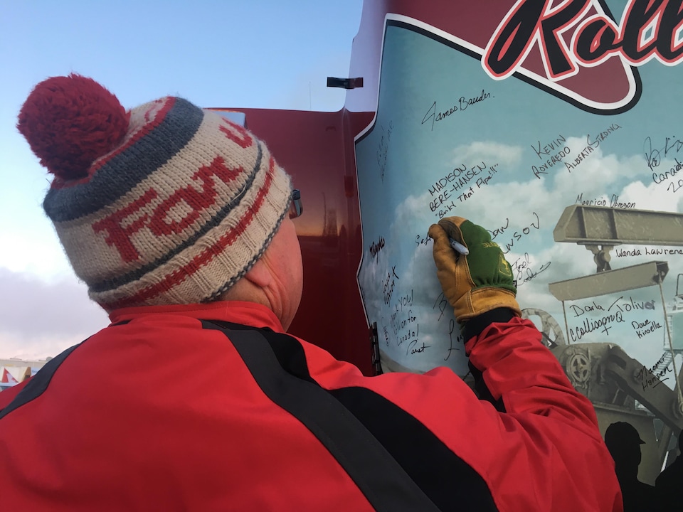 Un homme avec un bonnet est en train d'écrire un message de solidarité sur un camion.