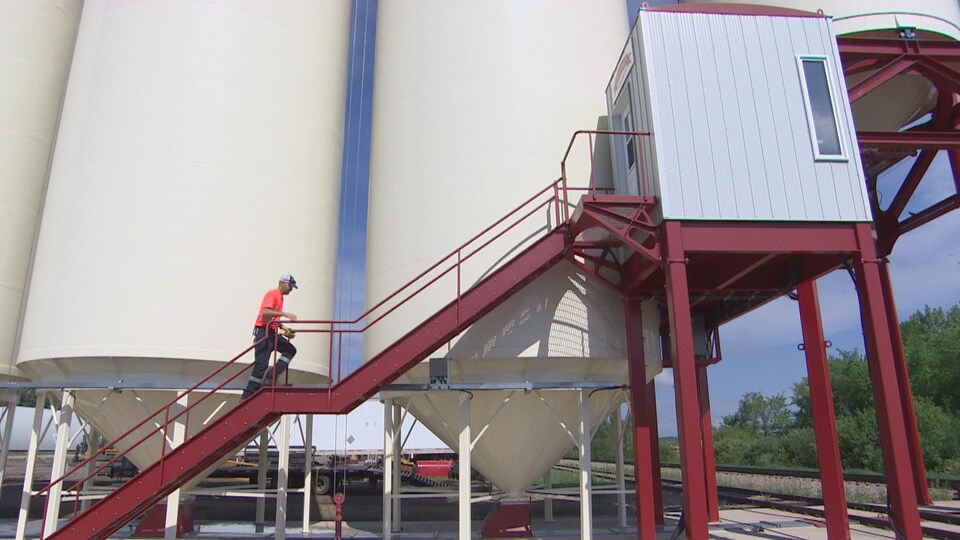 Les grands silos blancs. Au premier plan : un escalier rouge qui mène à la cabine de la station de chargement. Un homme monte les marches.
