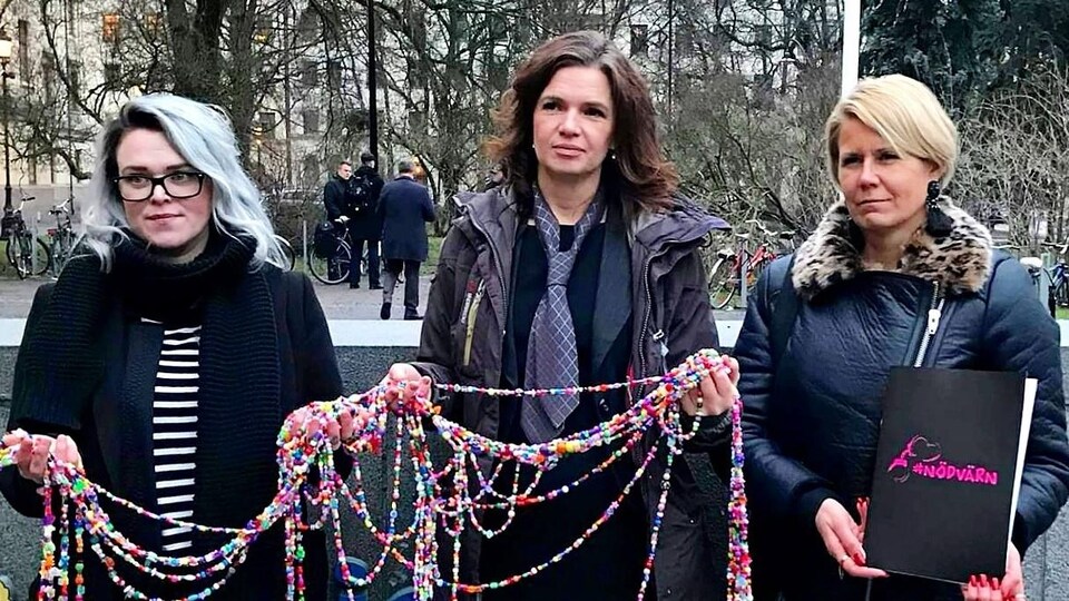 Trois femmes tiennent un collier de perles de couleur.