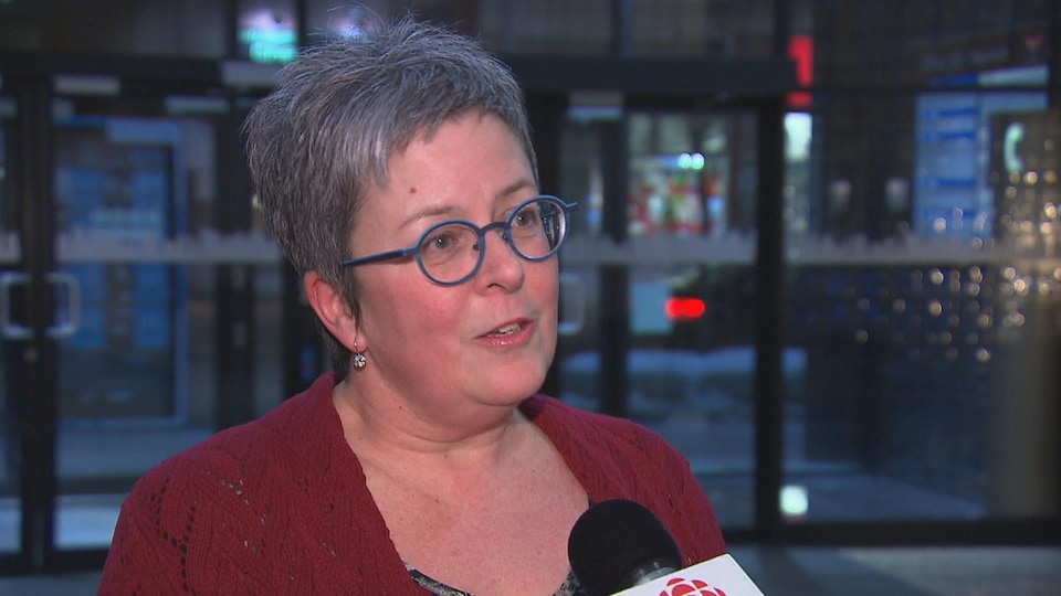 Une femme portant des lunettes bleues et un chandail rouge en entrevue au micro de Radio-Canada