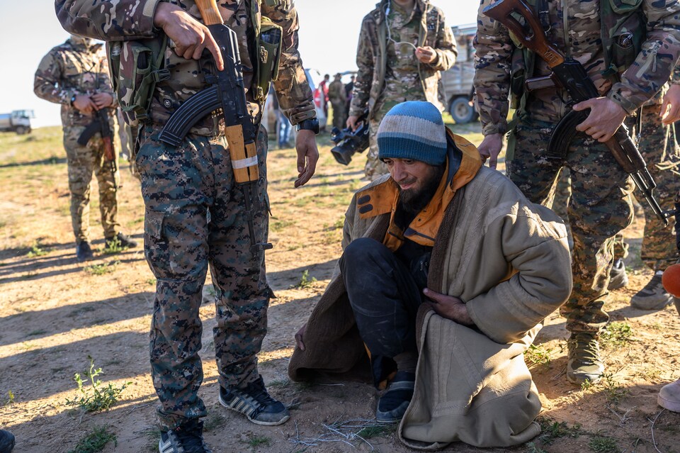 Un homme est accroupi devant des soldats armés.