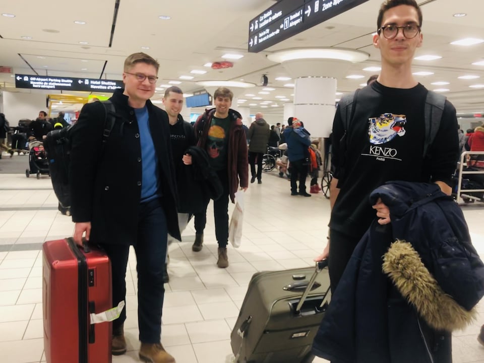 Quatre jeunes hommes souriants, avec leur valise.