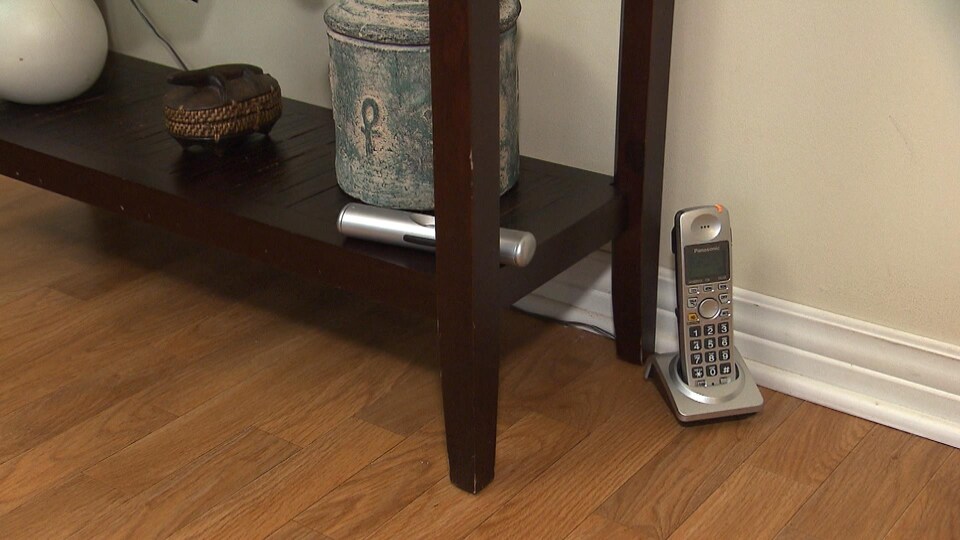 Un téléphone sans fil est posé sur son socle directement sur le plancher d'un appartement à côté d'une étagère en bois.
