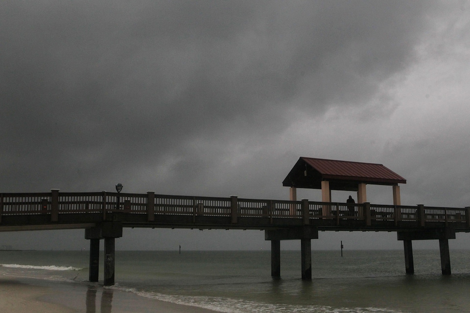 Une passerelle sur une plage devant des nuages d'un gris foncé.