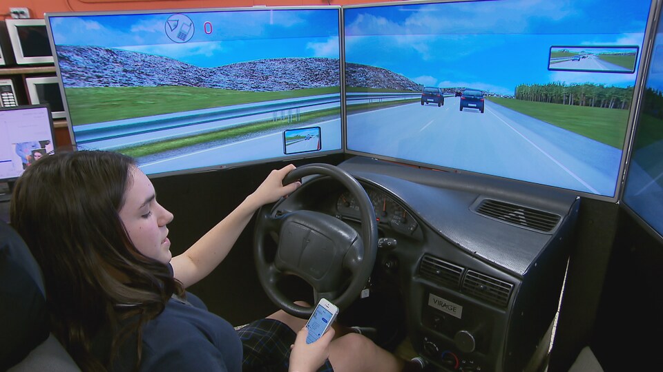 Une adolescente conduit sur un simulateur en tenant un cellulaire. 