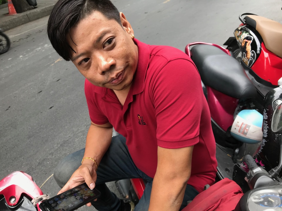 Un homme installé sur une moto avec un cellulaire en main.