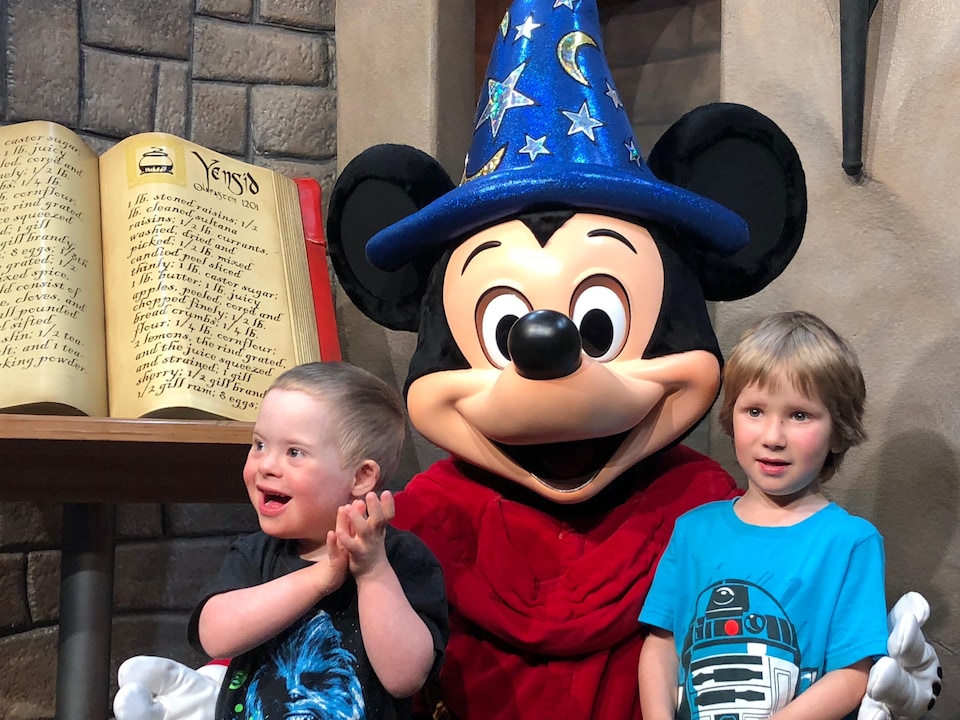 Deux enfants sourient à côté du personnage de Mickey Mouse.