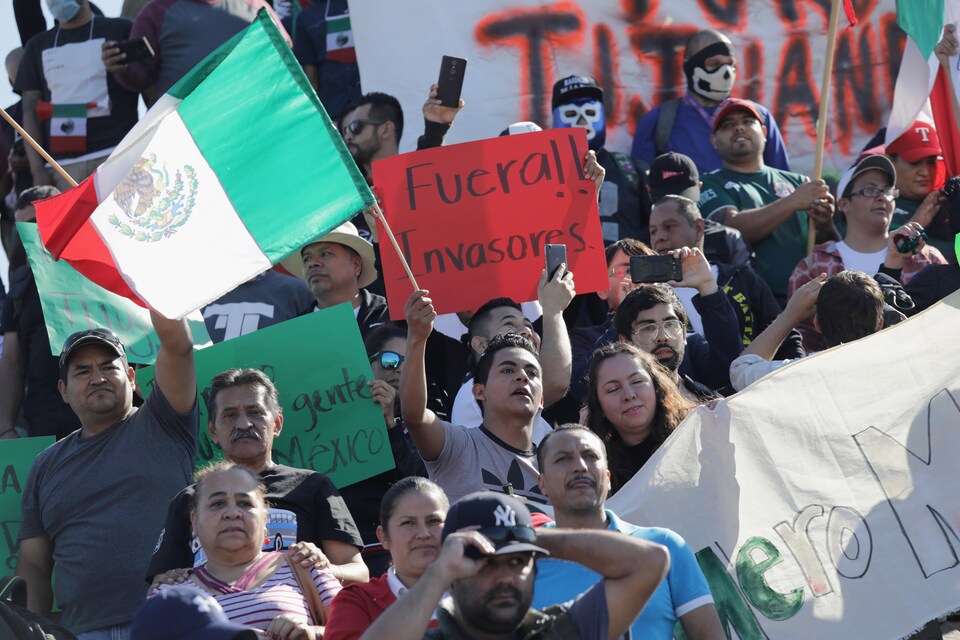 Des gens en groupe brandissent des drapeaux mexicains et des affiches anti-migrants.