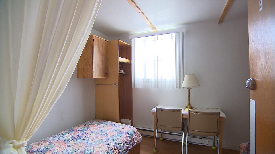 Vue à partir de la porte de la chambre numéro 4 de l'organisme Transit Sept-Îles avec lit simple, table pour lecture et petit garde-robe.