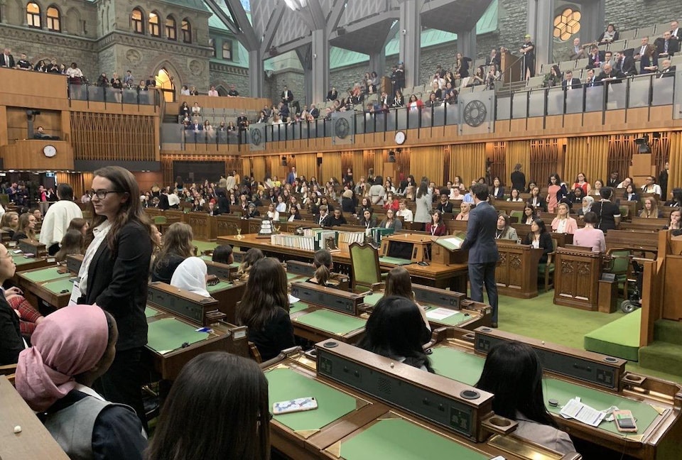 Une dizaine de femmes tournent le dos à Justin Trudeau, qui parle à la Chambre des communes. Des dizaines d'autres sont assises. 