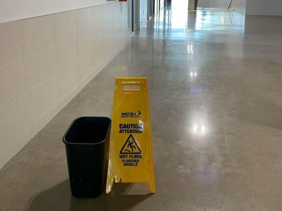 A black bin with a yellow sign next to it warning that the floor was wet.