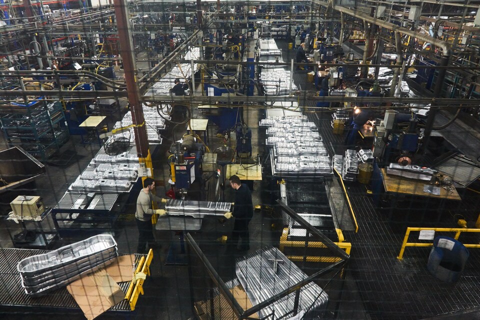 Vue de haut, à travers un grillage, d'employés qui travaillent à l'usine Spectra Premium de Boucherville.