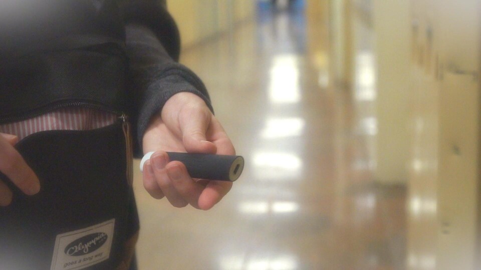 Une adolescente tient une cigarette électronique dans un corridor d'école.