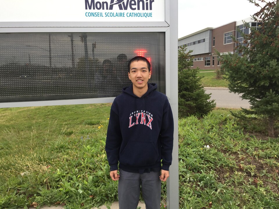 Photo de William devant le panneau de l'école