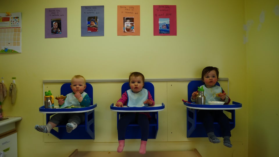 Trois enfants mangent dans des chaises accrochées au mur.