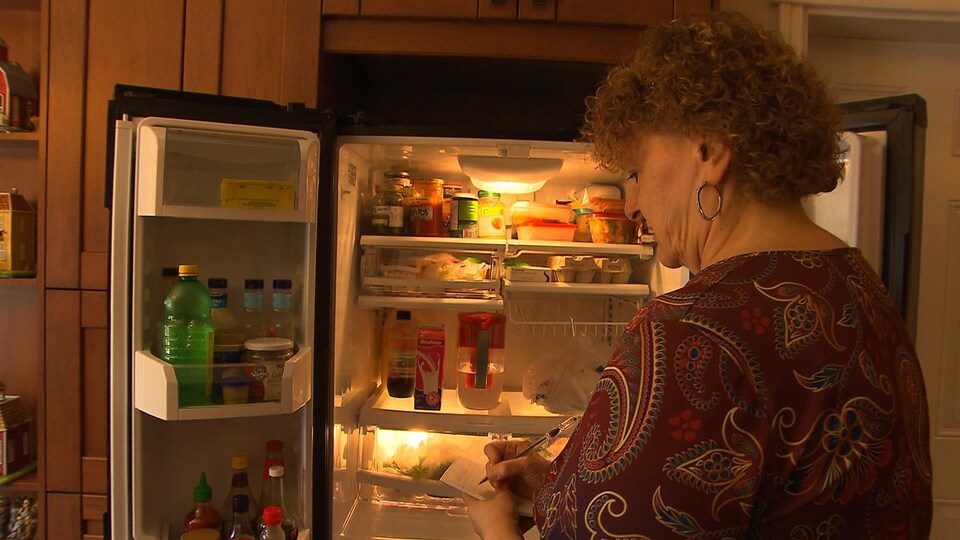 Une femme prend des notes en regardant l'intérieur d'un frigo.