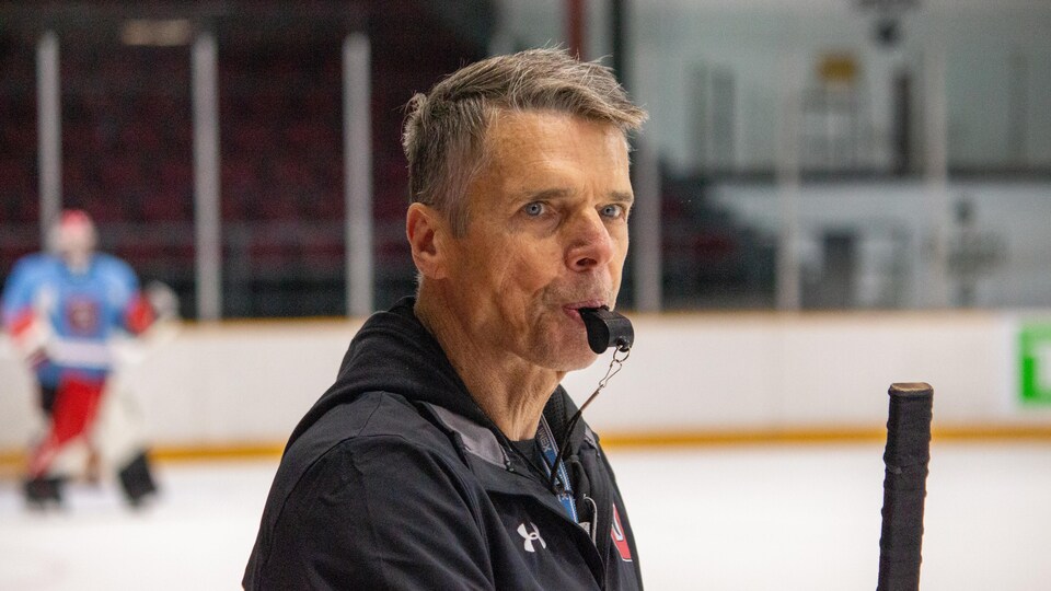 Un entraîneur de hockey siffle l'arrêt d'un exercice pendant un entraînement.