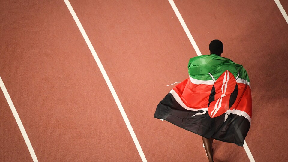 Arborant le drapeau du Kenya, l'athlète marche sur la piste.