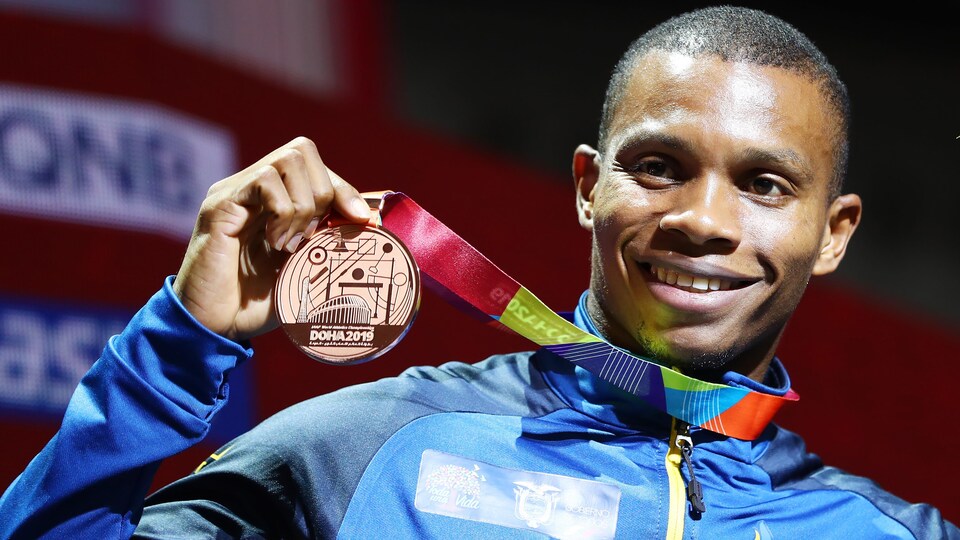 Alex Quinonez tient sa médaille de bronze bien haut de la main droite et un bouquet de fleurs de la main gauche.