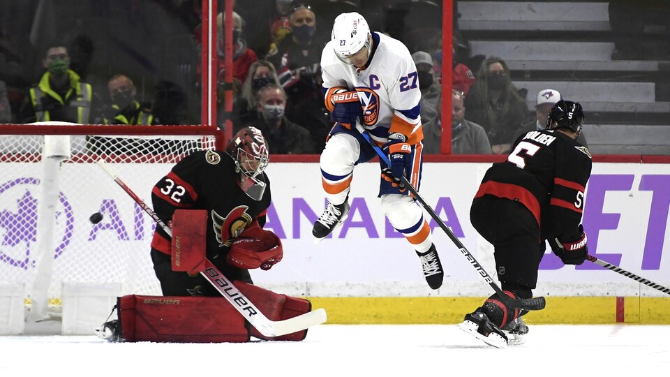 Un joueur de hockey saute dans les airs alors qu'un gardien tente d'arrêter une rondelle.