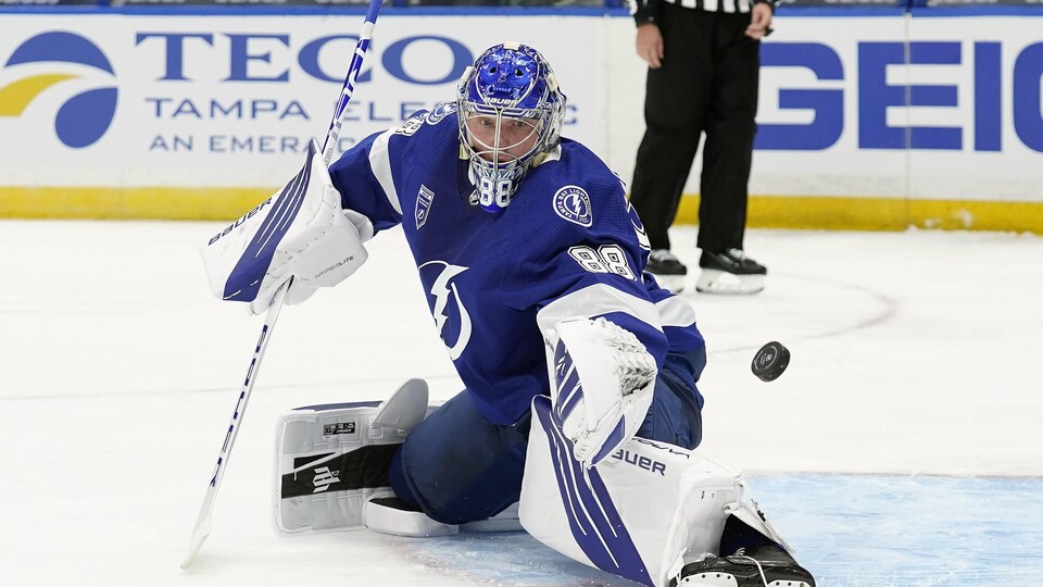 A kneeling goaltender looking at the puck in front of him.