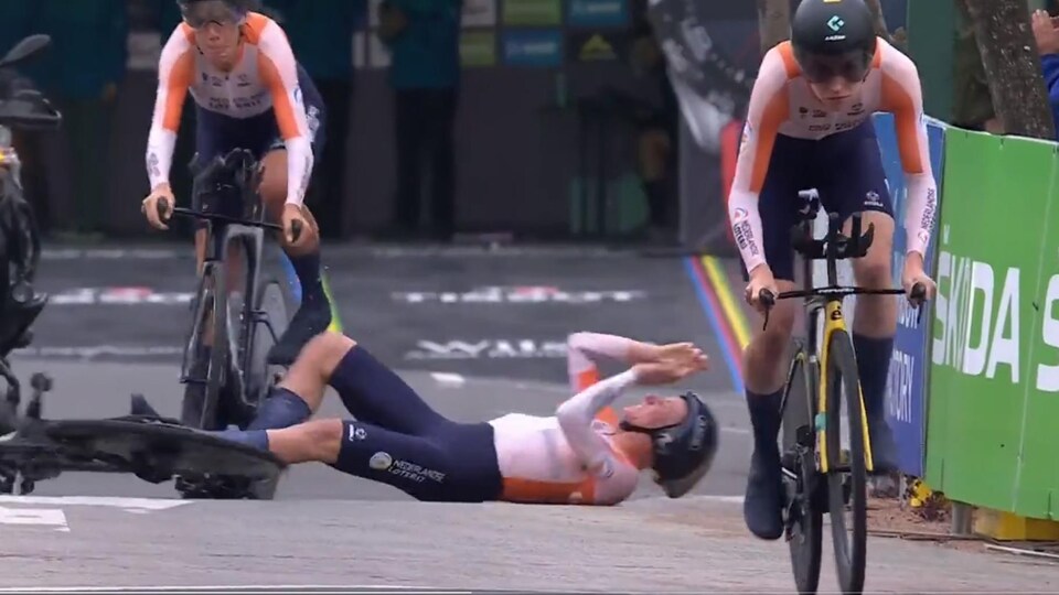 Une cycliste casquée est par terre après une chute, deux membres de son équipe continuent de rouler.