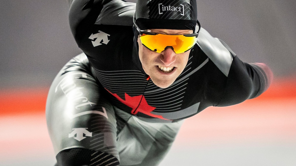 Antoine Gelinas-Beaulieu est en train d'effectuer sa course de patinage de vitesse, il serre les dents et porte des lunettes.